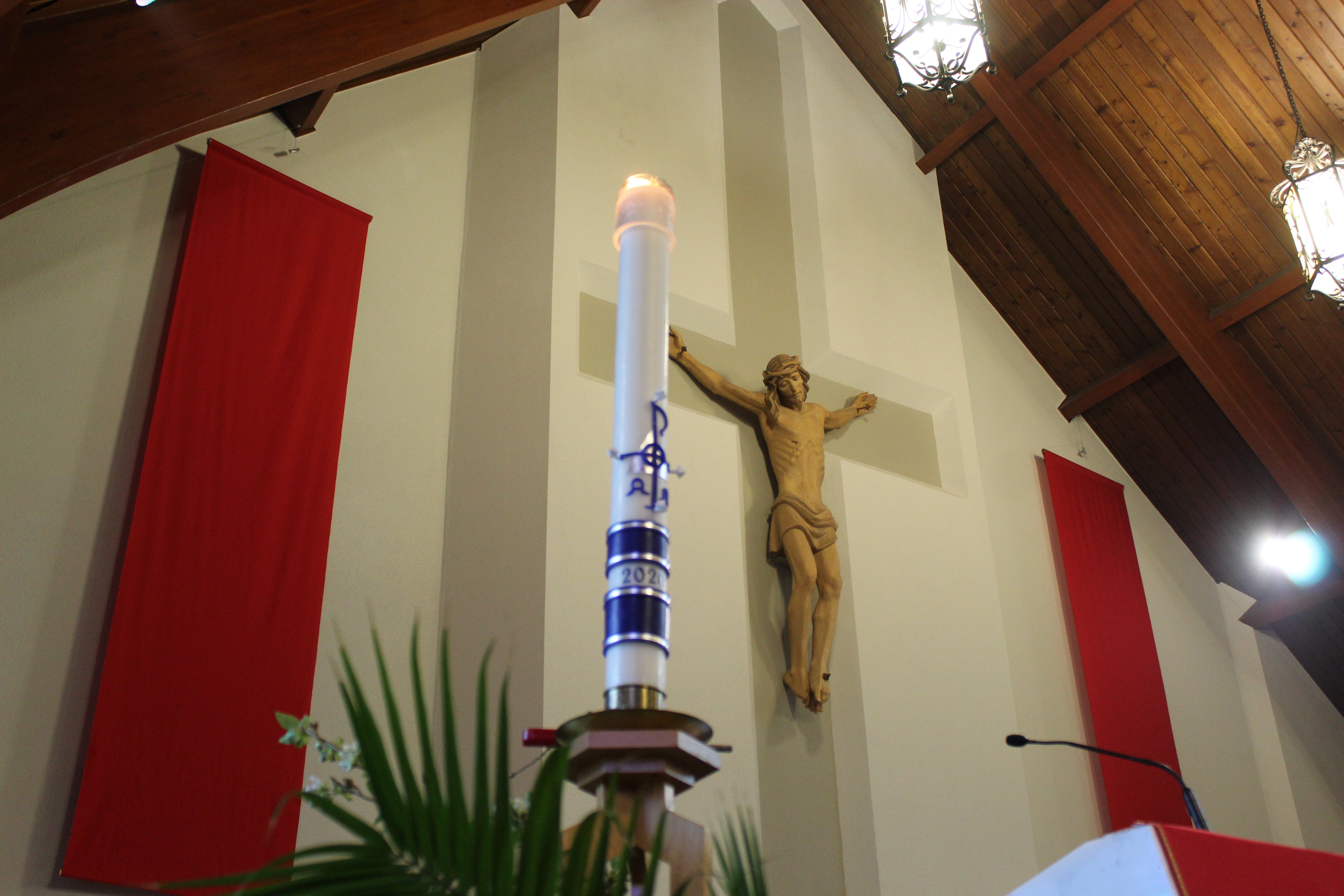 Image of the Main Crucifix of St. Jude's with red banners on each side of the crucifix, with the paschal candle also in frame, the photo taken from the left side of the sanctuary.